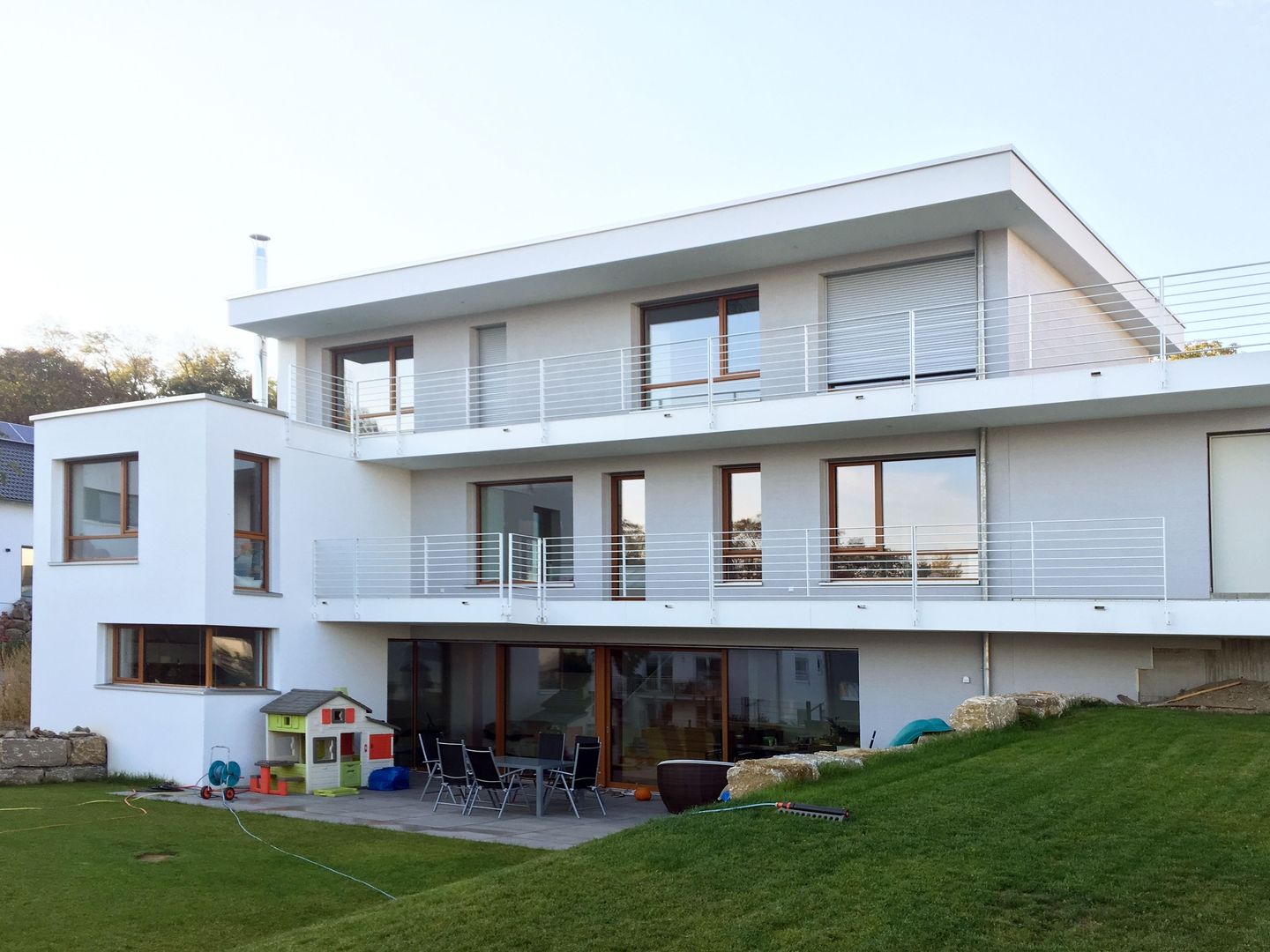 Einfamilienhaus L in Bruchsal: Rückansicht mit Balkonen, großer Terrasse und Garten am Hanggrundstück
